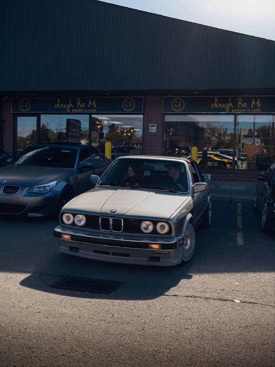 White BMW E30 parked in front of the Dough Re Mi storefront